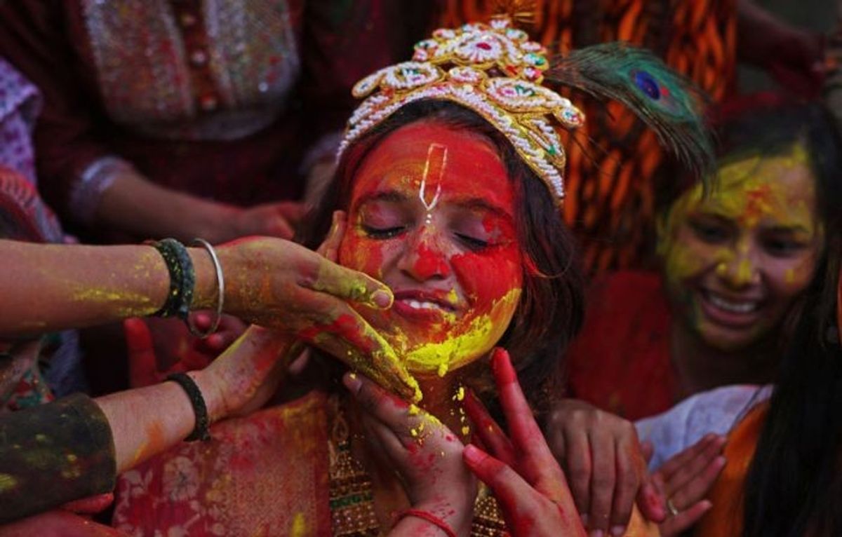 A girl dressed up as Lord Krishna gets her face smeared with colours during celebrations of the Hindu festival of 'Holi' in Varanasi in Uttar Pradesh state
