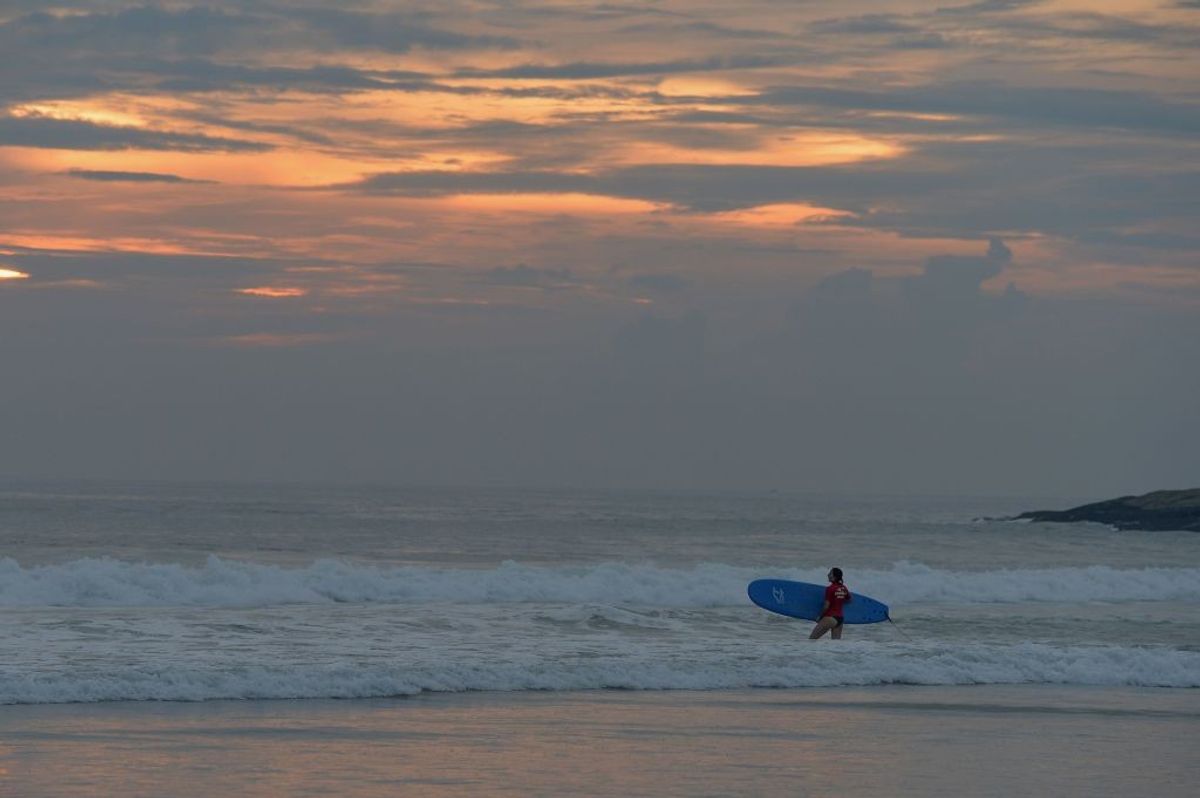 A tourist surfs in the Arabian sea during sunset at Kovalam Beach in Thiruvananthapuram, Kerala.