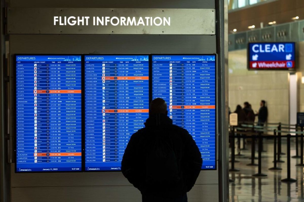 A traveller looks at a flight information display listing cancelled and delayed flights due to an FAA outage in the US