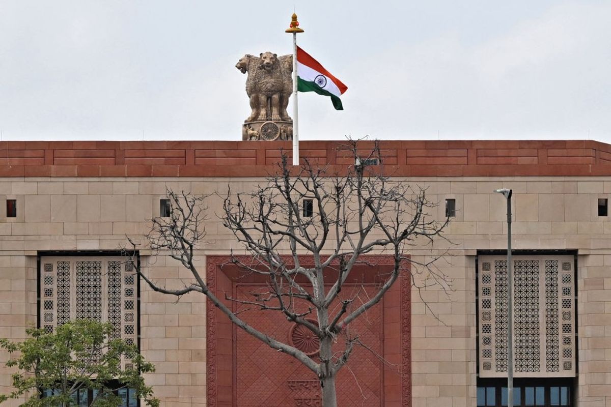 India's national flag flaps next to the 'National Emblem' at new parliament building.