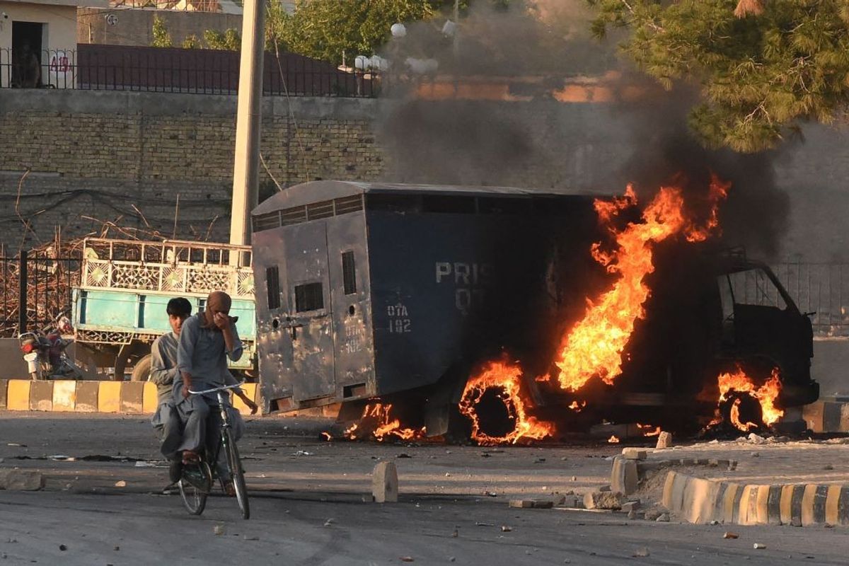Men on a bike ride past a burning police vehicle during a protest by Pakistan Tehreek-e-Insaf party activists and supporters of Pakistan's former prime minister Imran against the arrest of their leader, in Quetta