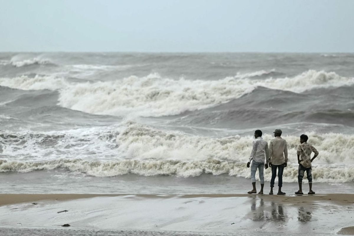 Men stand ashore while waves lash over the Kovalam beach as cyclone Michaung is expected to make landfall in Chennai in the southern Indian state of Tamil Nadu