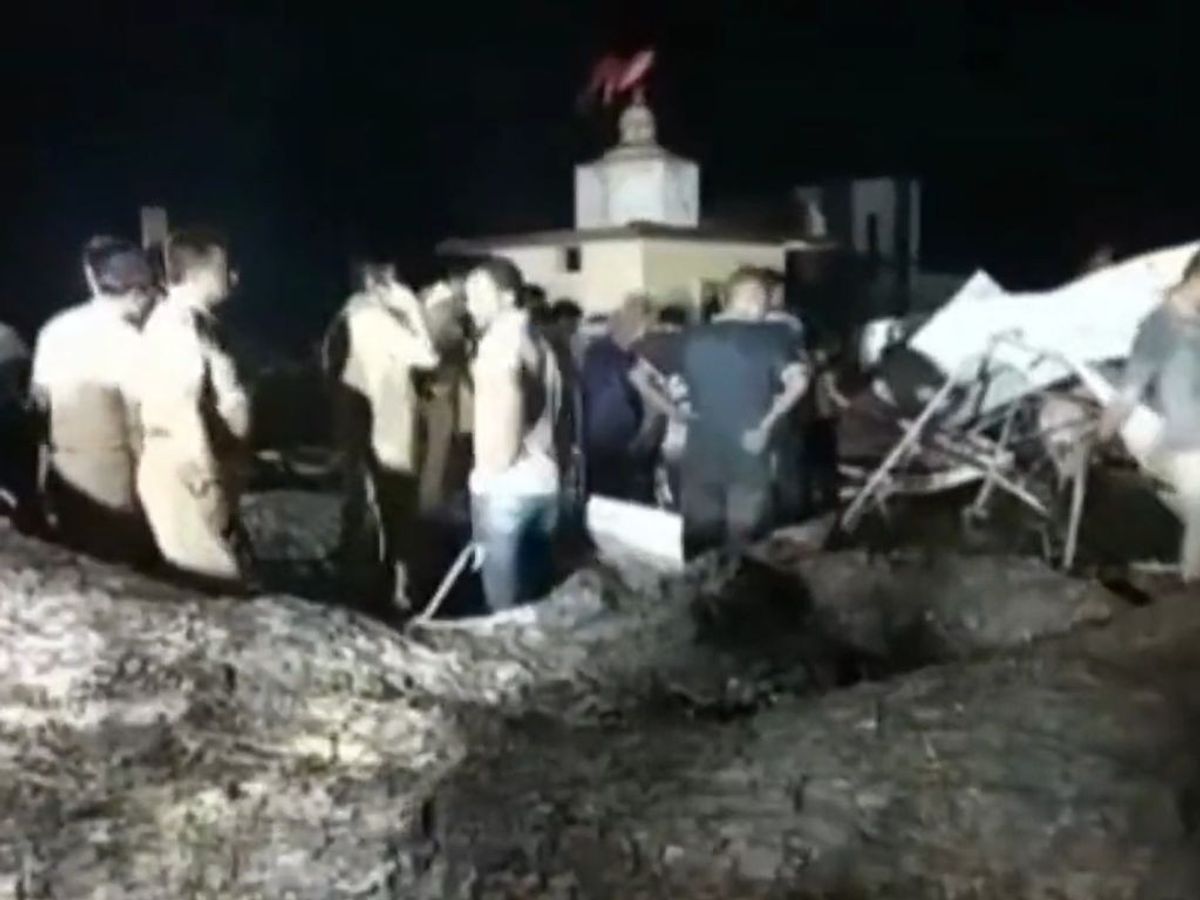 People stand at the spot where an old tree fell on a tin roof at a temple in Akola district of the western Indian state of Maharashtra, killing seven people and injuring 37,