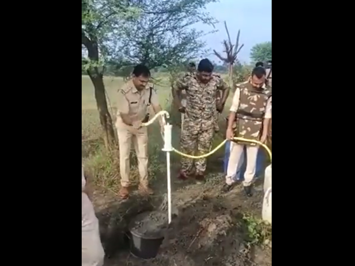 Police personnel pump out liquor from an underground drum filled with liquor in Madhya Pradesh