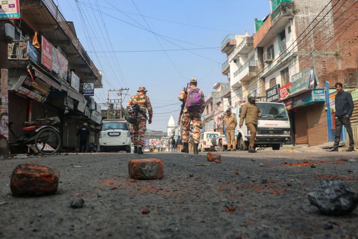 Security personnel walk past bricks and stones scattered on a road, a day after the religious clashes sparked following the destruction of a madrassa in India's Uttarakhand